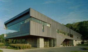 An exterior showcasing the exterior build made up of a mix of metal, stone, and glass surrounded by beautiful greenery