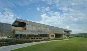 Blessings Golf Clubhouse exterior of metal, glass, and stone overlooking lush freshly manicured grass