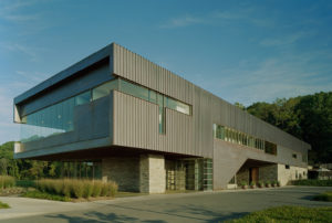 An exterior showcasing the exterior build made up of a mix of metal, stone, and glass surrounded by beautiful greenery