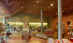 Well-lit shop space featuring modern wooden shelving, concrete pillars, descending hanging lights, enveloped in the walls and ceiling made of cherry plywood ribs