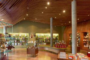Well-lit shop space featuring modern wooden shelving, concrete pillars, descending hanging lights, enveloped in the walls and ceiling made of cherry plywood ribs