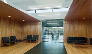 Interior airy wooden seating area below second flow overlooks with white ceiling and natural lighting