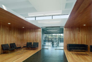 Interior airy wooden seating area below second flow overlooks with white ceiling and natural lighting