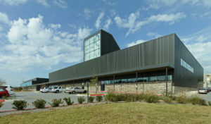 Metal and stone building exterior featuring a large window displaying 'FHS' to the street to the South