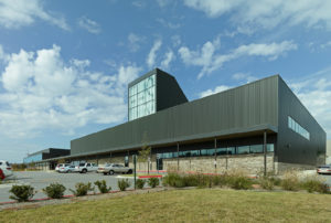 Metal and stone building exterior featuring a large window displaying 'FHS' to the street to the South