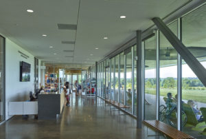 Visitor Center interior looks out through large glass windows to people in folding chairs enjoying the space