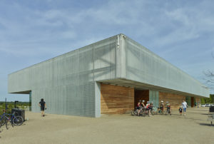 People on bikes gather by the center before a ride in the shade of the building