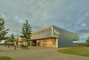 Walkway-facing side of the center with metal and wooden accents during sunset as a couple sits on a bench by the front entrance