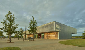 Walkway-facing side of the center with metal and wooden accents during sunset as a couple sits on a bench by the front entrance