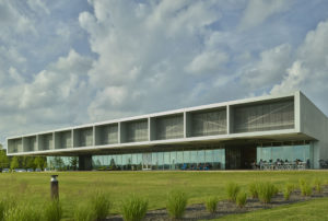 The structure of glass and aluminum bar grate materials contrasted with landscaping and cloudy blue sky