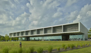 The structure of glass and aluminum bar grate materials contrasted with landscaping and cloudy blue sky