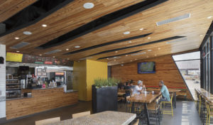 Dining room with large windows and sectional wooden ceilings hanging above men eating lunch