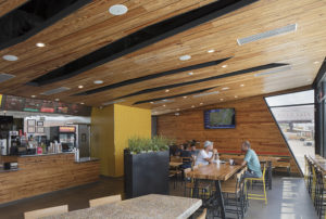 Dining room with large windows and sectional wooden ceilings hanging above men eating lunch