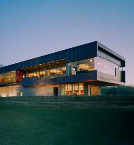 Blessings Golf Clubhouse seen at dusk lit from inside looking over the cut grass