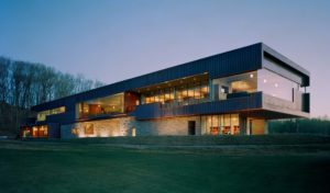 Blessings Golf Clubhouse seen at dusk lit from inside looking over the cut grass