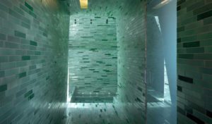 Greenish tiles line a large walk-in shower with frosted glass door