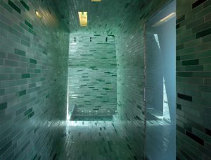 Greenish tiles line a large walk-in shower with frosted glass door