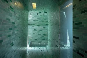 Greenish tiles line a large walk-in shower with frosted glass door
