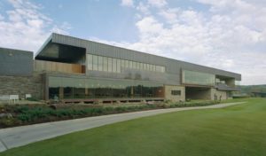 Blessings Golf Clubhouse exterior made of stone and metal next to a large grassy lawn