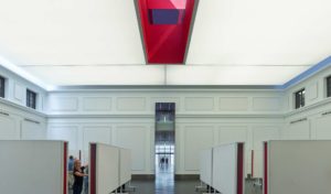 The red oculus skylight shines down to students working below in a large white room