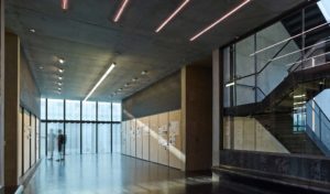 An interior shot the center made up of concrete, glass, and modern tube lighting along the ceilings