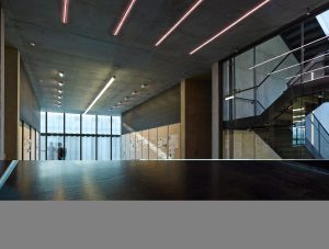 An interior shot the center made up of concrete, glass, and modern tube lighting along the ceilings