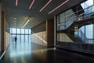 An interior shot the center made up of concrete, glass, and modern tube lighting along the ceilings