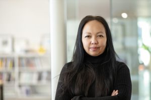 MBA team member headshot of Meryati Johari Blackwell with long black hair and a turtleneck sweater standing proudly with arms crossed