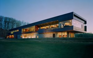 Blessings Golf Clubhouse seen at dusk lit from inside looking over the cut grass