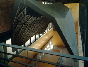 Looking down on a ‘shroud,’ clad in black zinc, suspended above a wooden conference room