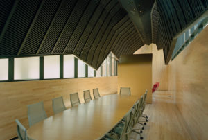 Wooden interior redesign of The Fullbright Building interior showcasing a ‘shroud,’ clad in black zinc, suspended above a wooden conference room