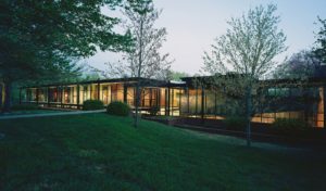 The Fulbright Building lit beautifully from inside seen through the landscaped lawn and trees