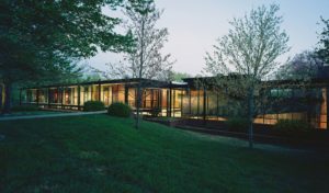 The Fulbright Building lit beautifully from inside seen through the landscaped lawn and trees