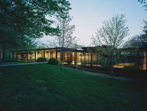 The Fulbright Building lit beautifully from inside seen through the landscaped lawn and trees