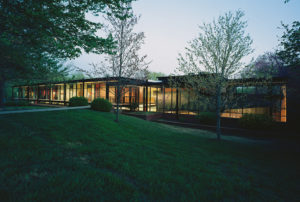 The Fulbright Building lit beautifully from inside seen through the landscaped lawn and trees