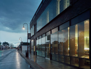 The building's exterior lit from inside at dusk during a rainstorm