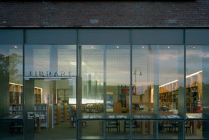 Gentry Public Library entrance of steel, brick, and glass looking in to modern wooden shelves filled with books