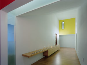 A view of a white wall and candle-lit hallway with a wood floor and yellow accent wall