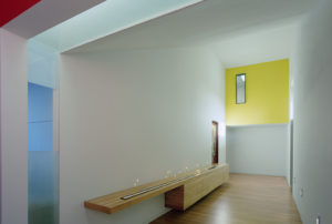 A view of a white wall and candle-lit hallway with a wood floor and yellow accent wall
