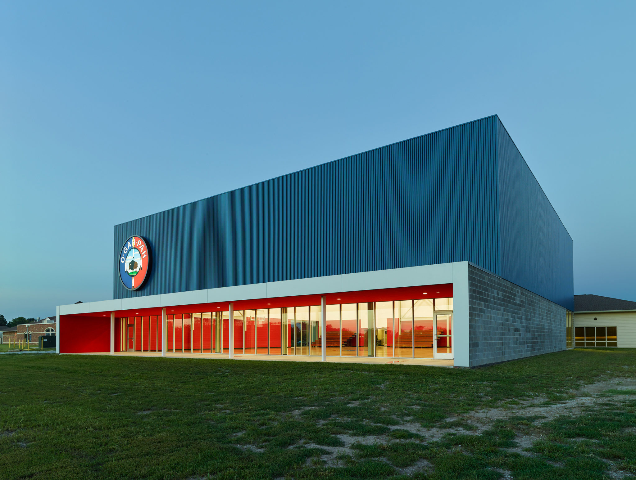 The exterior shows red stucco that spans the length of the gym with large blue volume, clad in a prefinished box rib panel