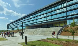 Library entrance shows metal and glass walls overlooking concrete steps and gathering students