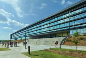 Library entrance shows metal and glass walls overlooking concrete steps and gathering students