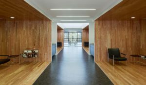 Interior airy wooden seating area below second flow overlooks with white ceiling and natural lighting