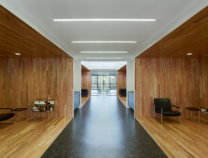 Interior airy wooden seating area below second flow overlooks with white ceiling and natural lighting