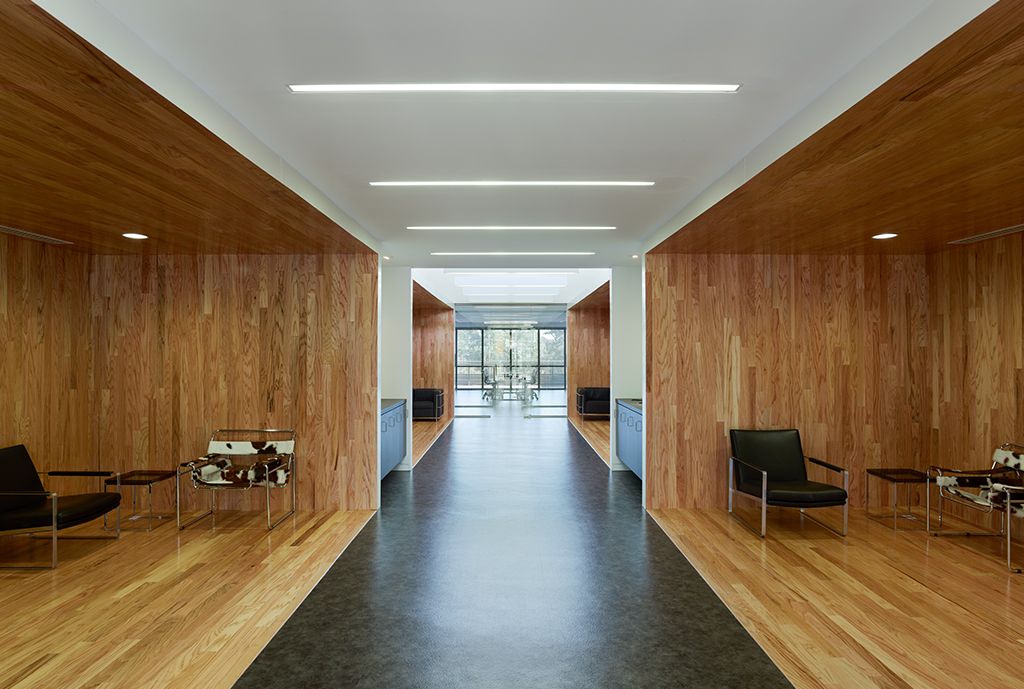 Interior airy wooden seating area below second flow overlooks with white ceiling and natural lighting