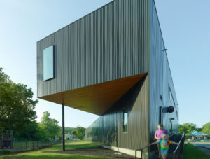 Box rib metal wall panel exterior facing the playground and a mother and daughter walk past