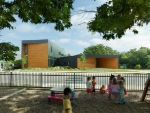 A view of the school from the play area just across the street, the silhouette of the building is surrounded by trees