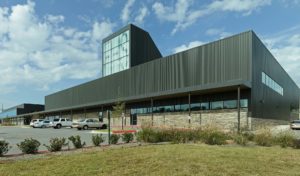 Metal and stone building exterior featuring a large window displaying 'FHS' to the street to the South