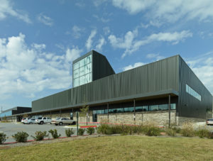 Metal and stone building exterior featuring a large window displaying 'FHS' to the street to the South