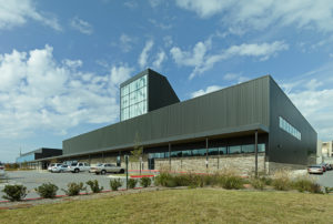 Metal and stone building exterior featuring a large window displaying 'FHS' to the street to the South